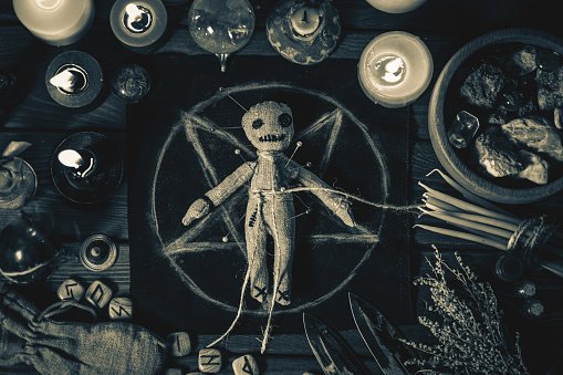 Voodoo Magic concept. Voodoo doll studded with needles with pierced rag heart on pentagram and around burning candles. Spooky or eerie magical esoteric ritual, black and white photo.