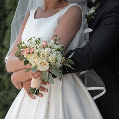 bride holds a wedding bouquet in hands, the groom hugs her from behind