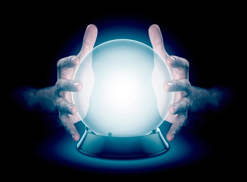 A pair of male hands surrounding a crystal ball conjuring up a hologram on an isolated dark studio background